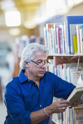 Älterer hispanischer Mann liest ein Buch in einer Bibliothek - BLEF13333