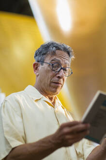 Älterer kaukasischer Mann liest ein Buch in einer Bibliothek - BLEF13334