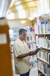 Älterer kaukasischer Mann liest ein Buch in einer Bibliothek - BLEF13335