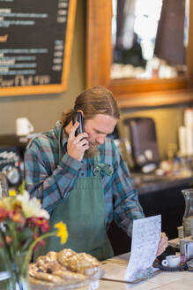 Kaukasische Bedienung am Telefon mit Klemmbrett in einem Cafe - BLEF13347