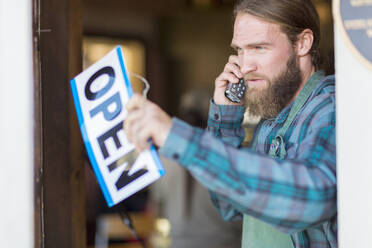 Caucasian server on telephone hanging open sign on cafe window - BLEF13360