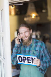 Caucasian server on telephone hanging open sign on cafe window - BLEF13361