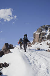 Hispanic hikers walking on snowy mountain - BLEF13373