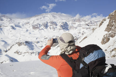 Hispanischer Wanderer fotografiert verschneite Bergkette, lizenzfreies Stockfoto