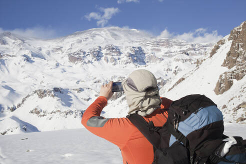 Hispanischer Wanderer fotografiert verschneite Bergkette - BLEF13375