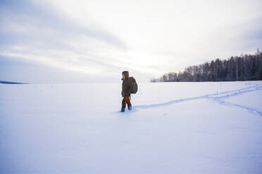 Mixed race man walking in snowy field - BLEF13396