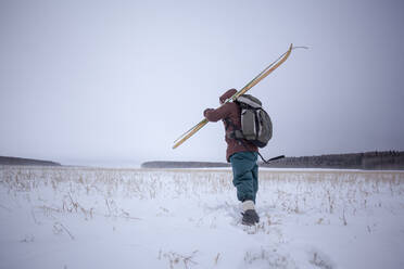 Gemischtrassiger Mann trägt Skier in einem verschneiten Feld - BLEF13397