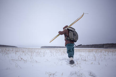 Mixed race man carrying skis in snowy field - BLEF13397