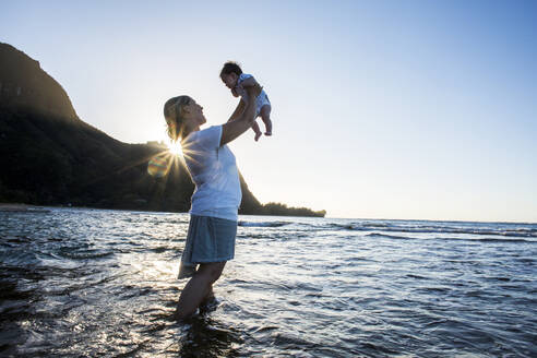 Caucasian mother holding baby in ocean on beach - BLEF13419