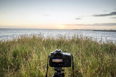 Nahaufnahme einer Kamera, die einen Sonnenuntergang über dem Meer fotografiert - BLEF13421