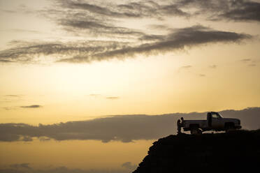 Silhouette von Menschen sitzen auf Pickup-Truck auf Klippe bei Sonnenuntergang - BLEF13422