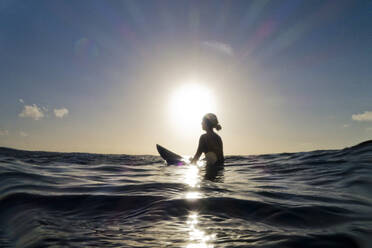 Silhouette of surfer sitting on surfboard in ocean - BLEF13435