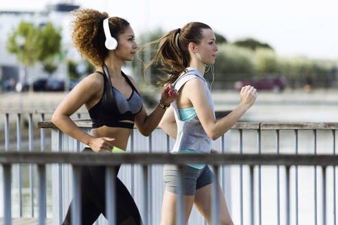 Zwei sportliche junge Frauen laufen auf einer Brücke - JSRF00480