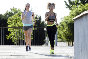 Zwei sportliche junge Frauen laufen auf einer Brücke - JSRF00481