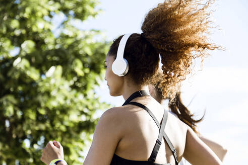 Sportliche Frau mit Kopfhörern beim Laufen - JSRF00483