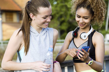 Zwei lächelnde sportliche junge Frauen überprüfen ihr Handy - JSRF00485