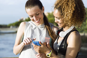 Zwei glückliche, sportliche junge Frauen prüfen ihr Handy - JSRF00492