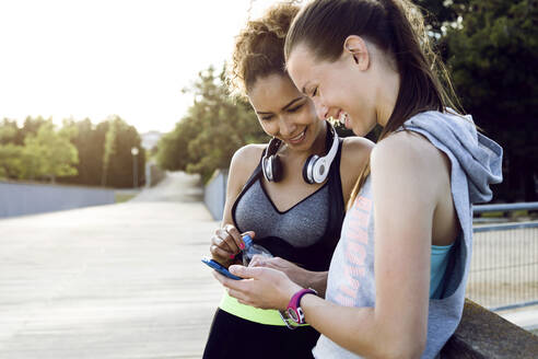 Zwei glückliche, sportliche junge Frauen prüfen ihr Handy - JSRF00493