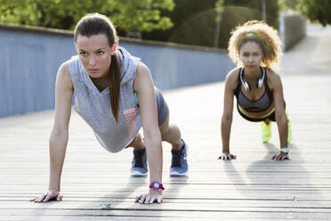 Two sporty young women doing push-ups on a bridge - JSRF00496