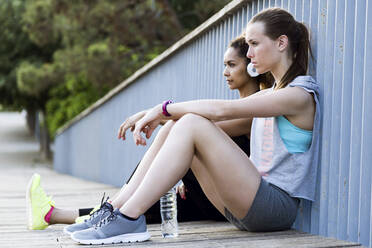 Zwei sportliche junge Frauen entspannen sich nach dem Training auf einer Brücke - JSRF00499