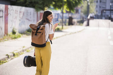 Young woman carrying violin case using cell phone on the street - UUF18379