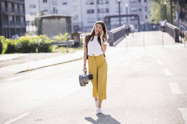 Young woman carrying violin case talking on the phone on the street - UUF18380