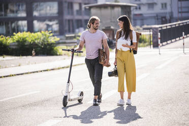 Young couple with electric scooter walking on the street - UUF18384