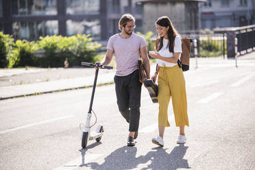 Young couple with electric scooter and smartphone walking on the street - UUF18385