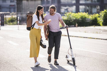 Junges Paar mit Elektroroller und Smartphone zu Fuß auf der Straße - UUF18386