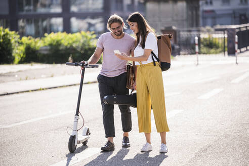 Junges Paar mit Elektroroller und Smartphone auf der Straße - UUF18387