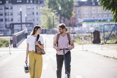 Junges Paar mit Elektroroller zu Fuß auf der Straße, lizenzfreies Stockfoto