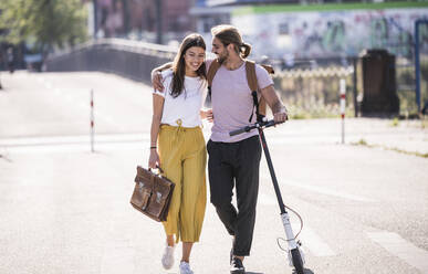 Young couple with electric scooter walking on the street - UUF18393