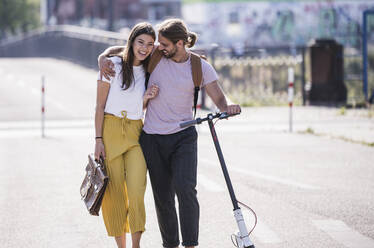 Young couple with electric scooter walking on the street - UUF18394