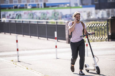 Junger Mann mit Elektroroller beim Telefonieren auf der Straße - UUF18403