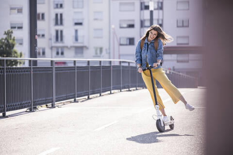 Glückliche junge Frau auf einem Elektroroller auf einer Brücke, lizenzfreies Stockfoto