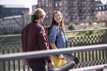 Glückliches junges Paar mit Skateboard auf einer Brücke - UUF18412