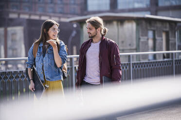 Young couple with skateboard and smartphone walking on a bridge - UUF18413