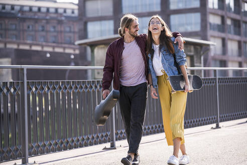 Glückliches junges Paar mit Skateboard auf einer Brücke - UUF18416
