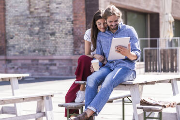 Young couple sitting on table in a beer garden looking at tablet - UUF18455