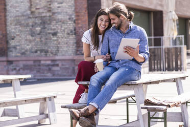 Happy young couple sitting on table in a beer garden with tablet - UUF18456