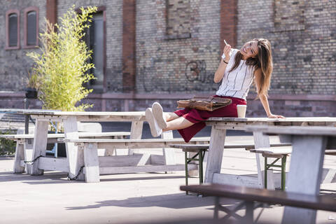 Young woman sitting on table in a beer garden using cell phone stock photo