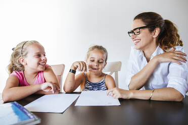 Happy teacher sitting at desk with two schoolgirls - LJF00575