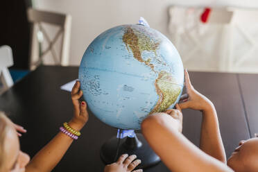 Close-up of two schoolgirls examining globe on desk - LJF00581