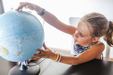 Curious schoolgirl looking at globe on desk - LJF00582