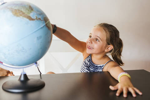 Glückliches Schulmädchen betrachtet Globus auf dem Schreibtisch, lizenzfreies Stockfoto