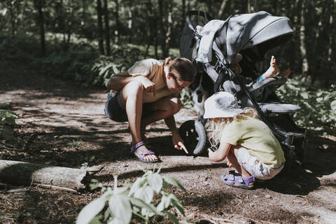 Mutter mit Tochter im Wald beobachtet einen Käfer auf dem Weg, lizenzfreies Stockfoto