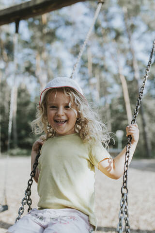 Porträt eines glücklichen Mädchens auf einer Schaukel auf einem Spielplatz, lizenzfreies Stockfoto