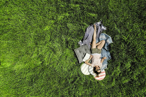 Draufsicht auf eine entspannte Frau mit Buch auf einer Wiese liegend - FMKF05763