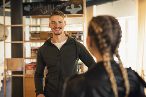 Trainer im Gespräch mit junger Frau an der Rezeption eines Fitnessstudios - SEBF00118