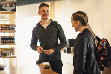 Young woman talking to coach at front desk of a gym - SEBF00120